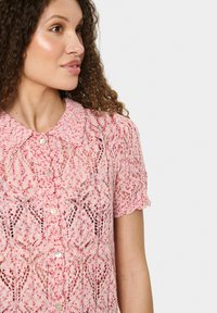Maglione lavorato a maglia rosa con motivo, maniche corte, dotato di colletto e chiusura con bottoni, che mette in mostra una texture e un design intricate simili a pizzo.