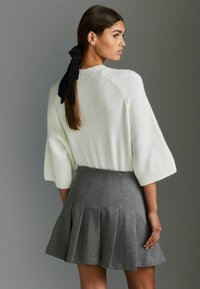 Pull en tricot crème avec des manches tombantes, associé à une jupe plissée grise. Inclus un ruban noir dans les cheveux, mettant en avant la texture et les détails de conception.