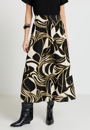 Donna che indossa un top nero, una gonna midi floreale bianca e nera con accenti dorati, stivaletti neri con punta appuntita e braccialetti neri e argento.