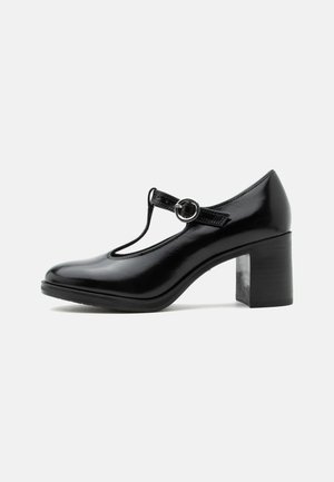 Chaussure Mary Jane en cuir verni noir avec bride en T, bout arrondi et talon épais sur fond blanc.