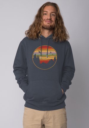Marineblauwe hoodie met een circulaire grafiek met gelaagde strepen in oranje, roze en groen, bergsilhouetten en vogels.