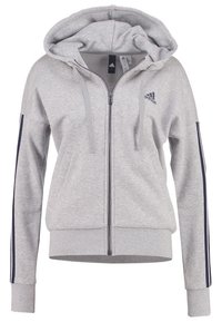 Felpa grigia con zip realizzata in un tessuto morbido. Presenta un cappuccio, tasche frontali e righe blu navy lungo le maniche. Logo Adidas sul petto.