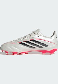 Chaussure de football argentée avec des rayures noires et des accents rose vif. Présente un design élégant, une tige texturée et des crampons coniques pour la traction.