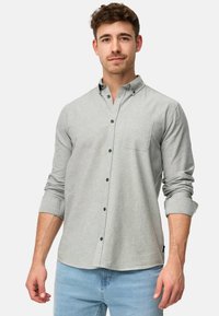 Camisa de botones gris con un bolsillo, con una textura suave, mangas largas recogidas en los puños y botones oscuros como acentos.