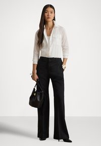 Camisa branca de botões com dois bolsos no peito, combinada com calças pretas de cintura alta. Os acessórios incluem uma mala preta e pulseiras douradas.