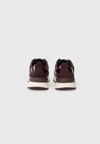 Un paio di sneakers bordeaux con suole bianche viste da dietro su uno sfondo bianco semplice.
