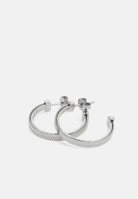 Orecchini a cerchio in argento con un motivo a zigzag testurizzato, con accenti quadrati e chiusura a perno. Il design è elegante e moderno.