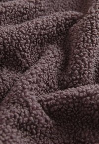 Lila, texturerad fleece med en mjuk, fluffig yta; har ett mycket texturerat, upphöjt mönster genom hela tyget.