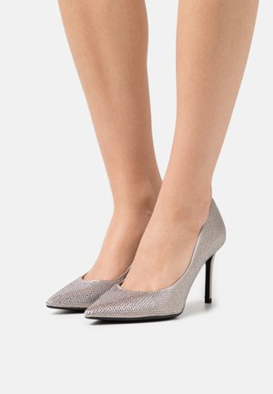 Sølv høje hæle med spids tå, som har en struktureret overflade udsmykket med små metalliske accenter og en slank sort stilettohæl.