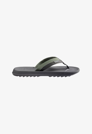Personne aux jambes croisées, portant des tongs grises et un short rose, assise sur une chaise en plastique rouge sur une terrasse extérieure carrelée.