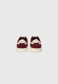 Sneakers in suede bordeaux con accenti crema, caratterizzati da un retro testurizzato e suole in gomma liscia, progettati per un uso casual.