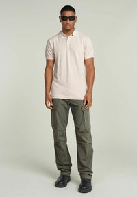 Polo in beige chiaro, in cotone, con maniche corte; abbinato a pantaloni cargo verde oliva con multiple tasche e una vestibilità ampia.
