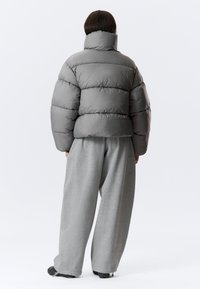 Sivá páperová bunda má vysoký golier, horizontálne švy a voľný strih, skombinovaná so sivými nohavicami s širokým strihom a textúrovanou obuvou.