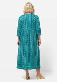 Vestido maxi en tono teal con mangas de tres cuartos, que presenta un patrón floral y rayas verticales. Falda acampanada, tejido ligero y escote redondo.
