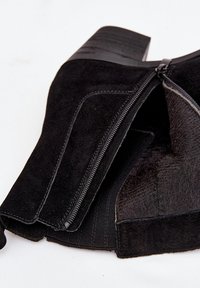 Bottine en daim noir avec fermeture éclair, finition texturée et talon bloc épais. Intérieur doublé d'un tissu doux pour plus de confort.