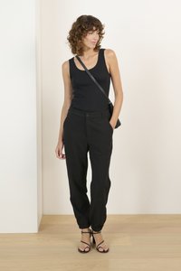 Black sleeveless top with textured pattern, paired with slim-fit black pants featuring elastic cuffs and pockets. Strappy black heels.