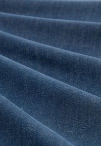 Denim tkanina tamno plave boje, s glatkom teksturom i suptilnim sjajem, prikazuje vertikalne nabore i uniformni uzorak.