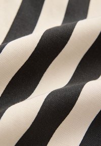 Zbliżenie na miękki materiał z szerokimi czarno-białymi poziomymi paskami, ukazujący szczegółową fakturę i delikatne fałdy.