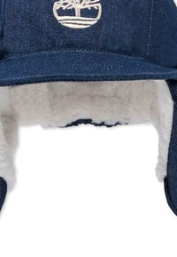 Berretto foderato in denim con orecchini, dotato di un interno in sherpa bianco e un logo ricamato sul davanti. Colore blu scuro con una finitura texturizzata.