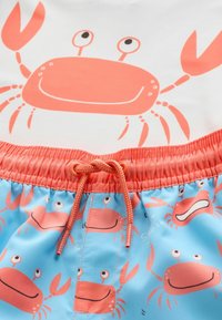 Pantaloni da bagno con base blu e motivi di granchi corallo; vita elastica con cordino regolabile. Tessuto morbido.