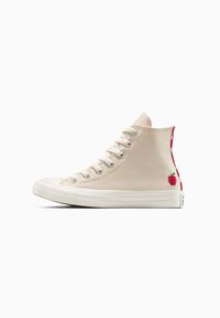 Zapatillas de lona estilo alto en beige con suela de goma blanca y puntera blanca. Presentan un detalle de fresa bordado en rojo en el costado y un talón en contraste.