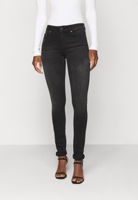 Jeans skinny pretos feitos de denim, com uma textura ligeiramente desbotada, design clássico de cinco bolsos e comprimento até ao tornozelo com punhos dobrados.