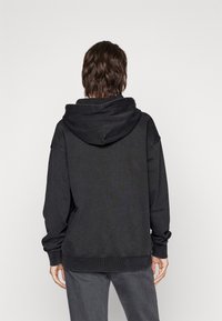 Hanorac negru cu glugă, cu o croială lejeră, textură moale, manșete și tiv ribbate. Prezintă o glugă mare la spate și un stil casual.