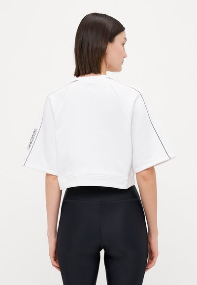 Vit kortärmad sweatshirt med avskuren midja, med en kontrasterande svart sömdekoration längs sömmarna. Textlogotyp på vänsterärm.
