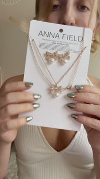 Rózsaarany ékszerszett, amely egy gyöngyökkel díszített nyakláncból és masni formájú fülbevalókból áll, márkás kártyán bemutatva.