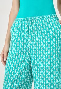 Pantalon large turquoise en tissu doux, orné d'un motif floral blanc répétitif et d'une taille élastique.