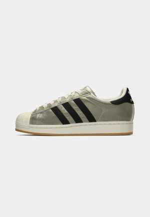 Adidas sportbačiai su metaliniu alyvuogių spalvos viršumi, trimis juodomis juostelėmis, guminėmis pirštų apsaugomis ir guminiu padu. Klasikinis dizainas su tekstūruota medžiaga.