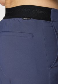 Navy athletic shorts with a black waistband featuring logo detail. Smooth fabric, elastic waist, and single back pocket with stitch accents.