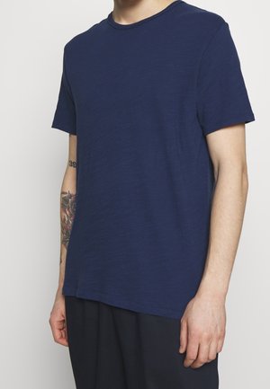 Granatowa koszulka z krótkim rękawem, uszyta z miękkiego, teksturowanego materiału, z okrągłym dekoltem, o luźnym kroju i minimalnych detalach szycia.