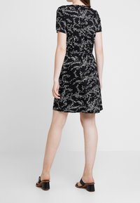 Svart klänning med vitt abstrakt mönster, korta ärmar, figurnära midja och utsvängd nederdel. Kombinerad med svarta klacksandaler.