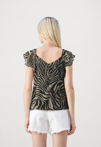 Svart og khaki zebramønstret topp med volangermer og V-back, laget av lett materiale, kombinert med hvite denimshorts.