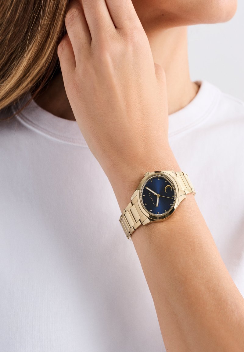 Kuldtooni kell sinise puutega, metallriba ja hõbedaste aktsentidega. Omab kuu faasi ekraani ja lihtsaid tunni markerid.