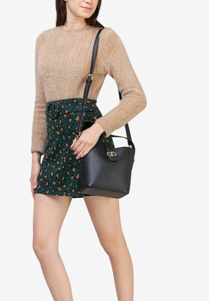 Sac à main en cuir noir avec une forme structurée, accents en métal doré et une bandoulière amovible, associé à un pull en laine beige texturé et une jupe à motifs.