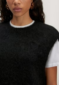Black fuzzy sweater with a crew neck, layered over a white T-shirt. Notable details include textured fabric and a simple, clean design.