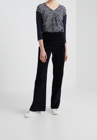 Navy-toppi, jossa on kukkakuosi ja 3/4-hihat, yhdistettynä korkeavyötäröisiin mustiin samettifarkkulegginsseihin ja valkoisiin tennareihin.