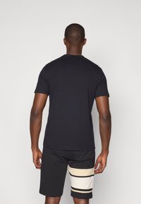 Camisa de algodón de manga corta negra, combinada con pantalones cortos negros que tienen rayas horizontales en beige y negro.