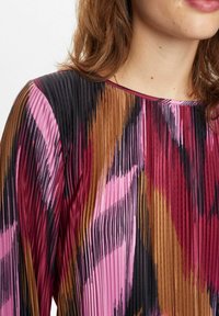 Savu svārku kleita, kas rotāta ar dzīvīgu rozā, melnā un brūnā krāsā. Gluda tekstūra ar apaļu kakla izgriezumu un garām piedurknēm.