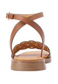 Sandali in pelle marrone con design a fascia incrociata, dettagli scallop ai lati e suola piatta in gomma. Texture liscia su tutta la superficie.