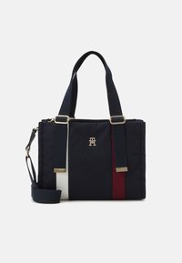 Granatowa torba na ramię z nylonu z czerwonymi i białymi paskami, złotymi elementami ozdobnymi, podwójnymi uchwytami u góry oraz odpinanym paskiem na ramię.