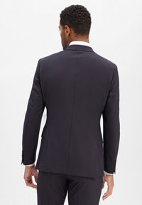 Marineblauwe blazer met een getailleerde pasvorm, enkele vent, en twee achterzakken. Glad stof met subtiele textuur en knoopmanchetten.