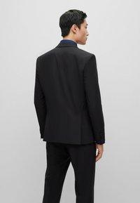 Giacca su misura nera con risvolti a punta, vestibilità slim, con fodera a motivo blu visibile nel colletto e nei polsini. Texture liscia.