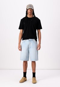 Black cotton t-shirt with short sleeves, light blue denim shorts, black socks, tan sneakers, and a light gray cap.