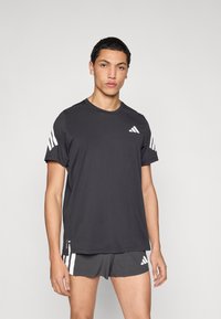 Must spordipluus lühikeste varrukatega, millel on valge Adidas logo ja kolm triipu õlgadel. Pehme, kerge kangas, ümara kaelusega.