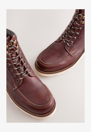 Pruunid nahast saapad siledapinna ja metallist silmuste, hallide paelte ning kreemika värvi kummitaldadega. Äärte ääres tikand detail.