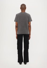 Camiseta gris de cuello redondo y mangas cortas, combinada con pantalones cargo negros que cuentan con bolsillos y dobladillos acampanados, vista desde atrás.