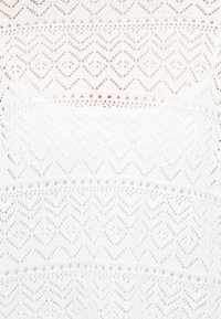 Λευκό ύφασμα με περίτεχνο δαντελένιο σχέδιο που περιλαμβάνει ζιγκ-ζαγκ και ρόμβους σε οριζόντιες ζώνες.